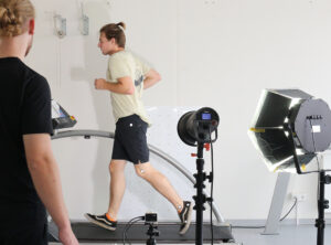 Zwei Bionik Studenten im Praktikumsversuch. Ein Student joggt auf einem Laufband und seine Beine werden von einer Kamera gefilmt. Ein weiterer Student ist dem Jogger zugewandt und sieht zu.