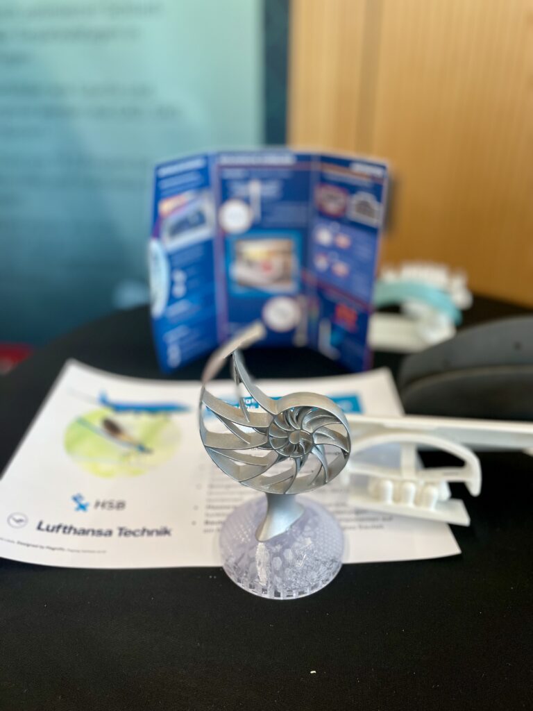 Der Pokal des Bre3DAwards auf dem Gewinnertisch. Im Hintergrund des Pokals liegen Anschauungsmaterialien des Projekts.