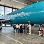 Eine Gruppe Menschen steht in einem Hangar vor einem blauen Flugzeug.