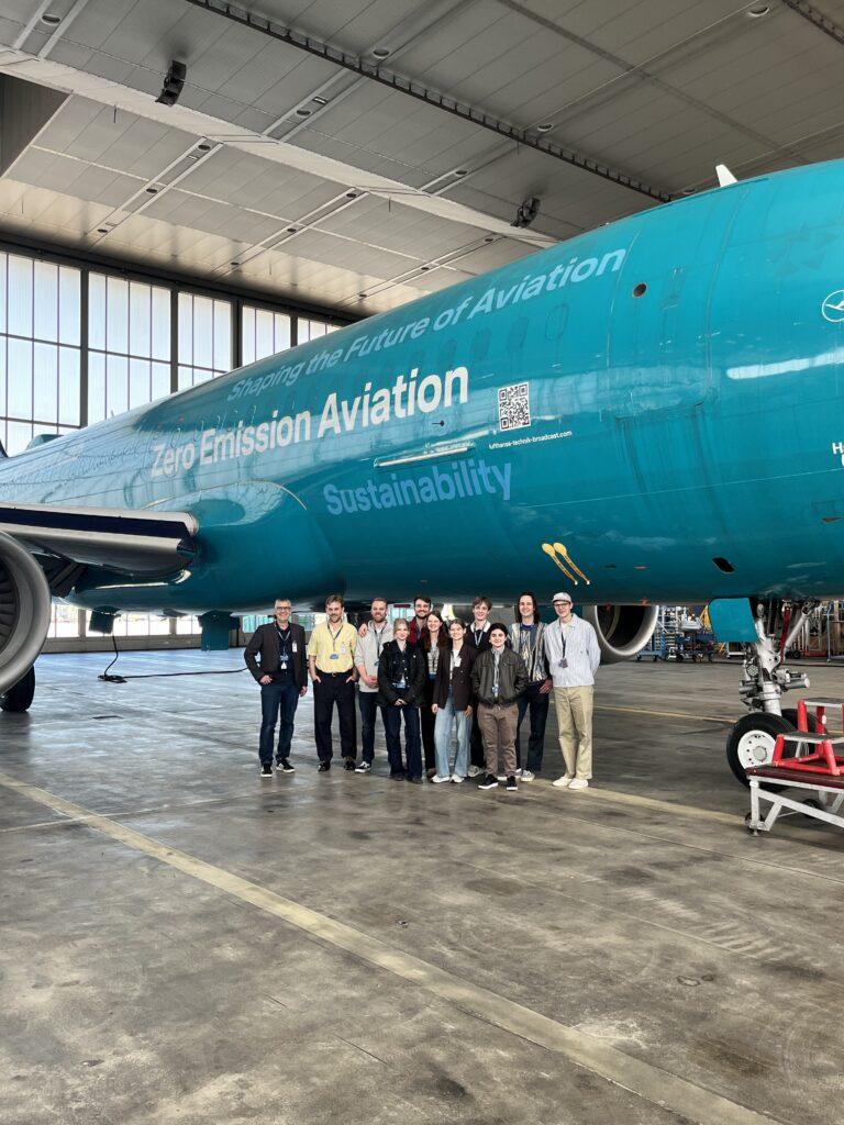 Eine Gruppe Menschen steht in einem Hangar vor einem blauen Flugzeug.